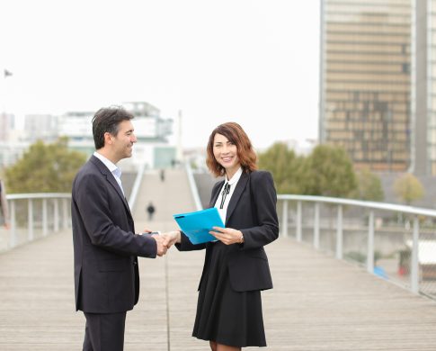 man with smartphone going towards woman with blue folder of documents, old IT business partners meet to discuss work. Middle-aged Americans in strict suits shaking hands smiling. Concept of innovative technologies, modern clothes or cooperation.